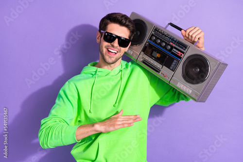 Portrait of handsome cheerful good mood guy brunet hairdo wear green hoodie hold boombox on shoulder isolated on violet color background