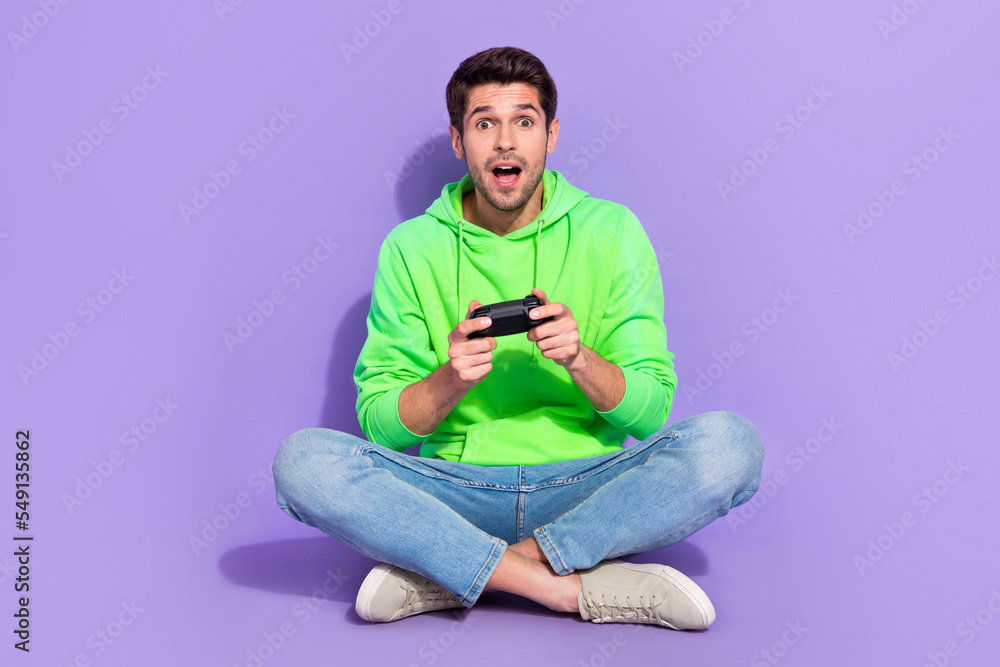 Full length photo of cheerful impressed guy dressed neon sweatshirt enjoying playstation isolated violet color background Full length photo of cheerful impressed guy dressed neon sweatshirt enjoying playstation isolated violet color background