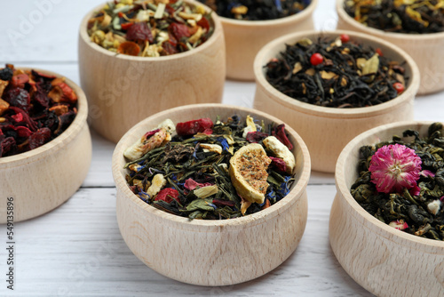 Different kinds of dry herbal tea in bowls on white wooden table