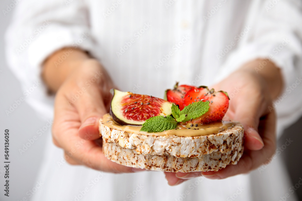 Woman holding tasty crispbreads with peanut butter, strawberries, mint and fig, closeup