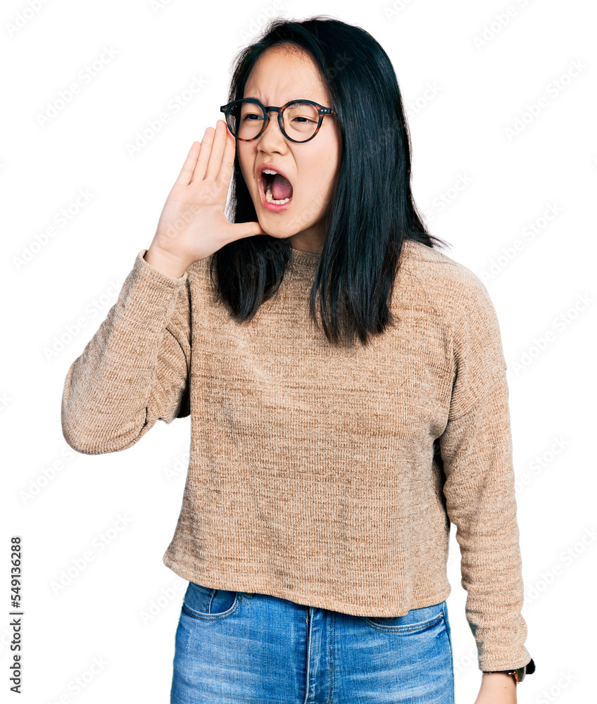 Young chinese woman wearing casual sweater and glasses shouting and screaming loud to side with hand on mouth. communication concept. Young chinese woman wearing casual sweater and glasses shouting and screaming loud to side with hand on mouth. communication concept.