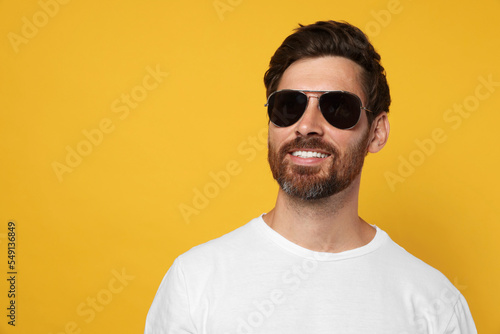 Portrait of smiling bearded man with stylish sunglasses on orange background. Space for text © New Africa
