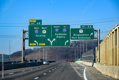 traffic and multiple traffic signs over the highway outside Binghamton in Upstate NY.  Heading West on Route 86 in NYS.