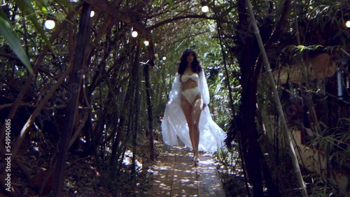 Gorgeous model in a white bikini and white dress walks through a jungle in slow motion photo