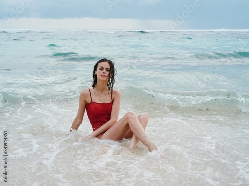 Fotografie, Obraz Woman tourist in red swimsuit sitting on the sand on the beach in the ocean in t