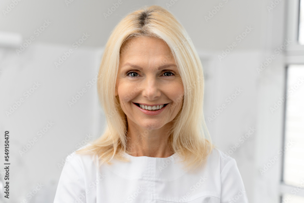 Waist up portrait of mature cosmetologist in white lab coat looking at the camera with smile