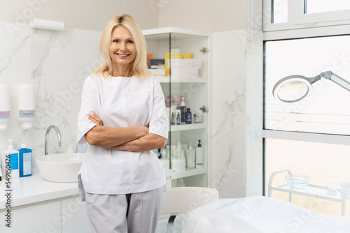 Portrait of mature cosmetologist in white lab coat looking at camera