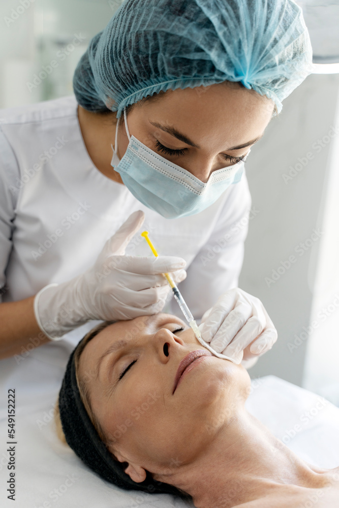 Beautician expert's hands injecting botox in senior female lips zone Beautician expert's hands injecting botox in senior female lips zone