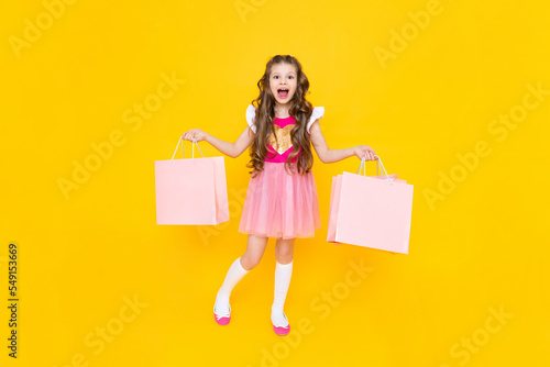 A little girl with full-length shopping. A fashionista after shopping on a yellow isolated background. Children's sale. The young princess is happy to make new purchases.