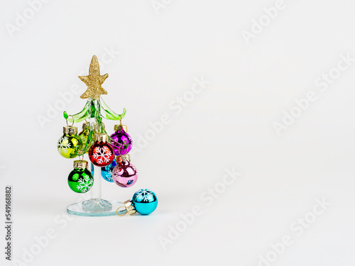 New Year's Eve photo with a glass Christmas tree, decorated with toys, standing on a white background. There is room for text.