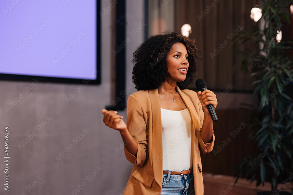 Fototapeta premium African businesswoman talking to the public over the microphone, giving the lecture.