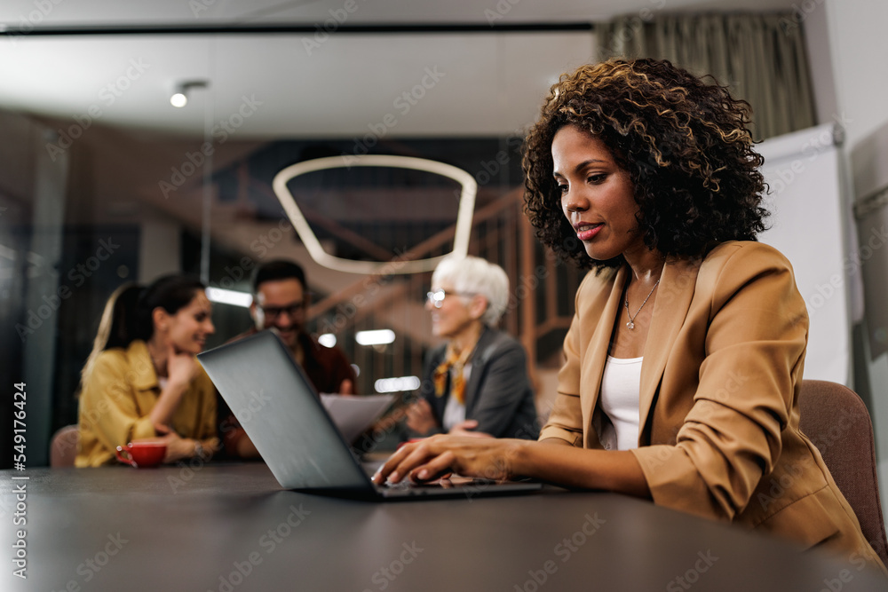 African woman working at the office, her colleagues sitting in the background. African woman working at the office, her colleagues sitting in the background.
