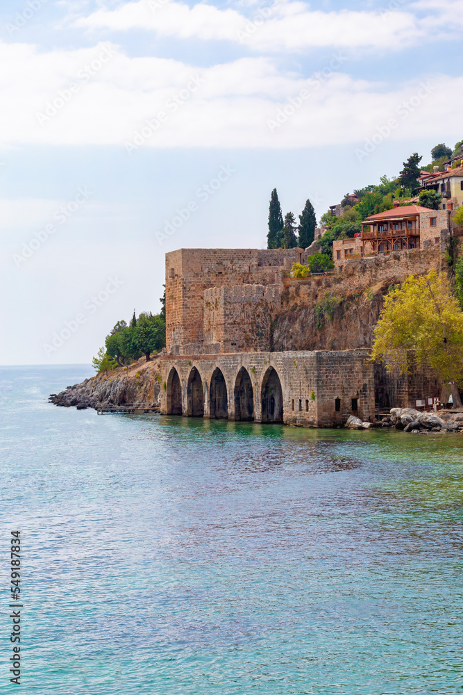 Alanya, Turkey (Turkiye). Ancient shipyard (Tersane) near of Kizil Kule tower. Famous tourist destination with high mountains. Part of medieval fortress (Alanya Castle) on the mountainside. Copy space