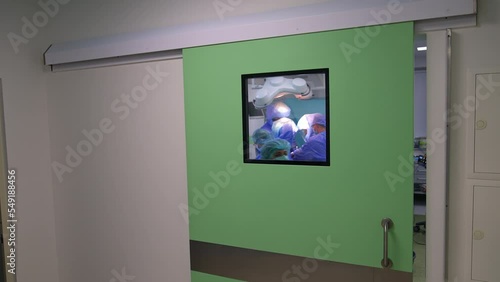 Sliding door with a window to the modern surgical room. Operation is taking place inside the ward. Nurse comes up to the door to close it. photo