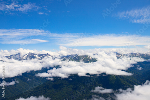 mountain landscape with blue sky above clouds, hilltops and natural green forests