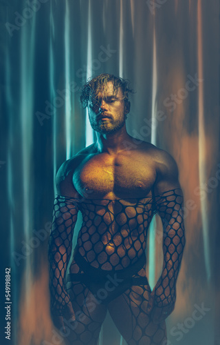 Фотография Multicolored creative artistic portrait of a sexy muscular young man with net outfit on a colorful rainbow lighting and background