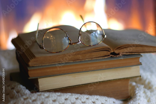 Stack of books, soft blanket, books and reading glasses on the table in front of a fireplace. Selective focus. photo