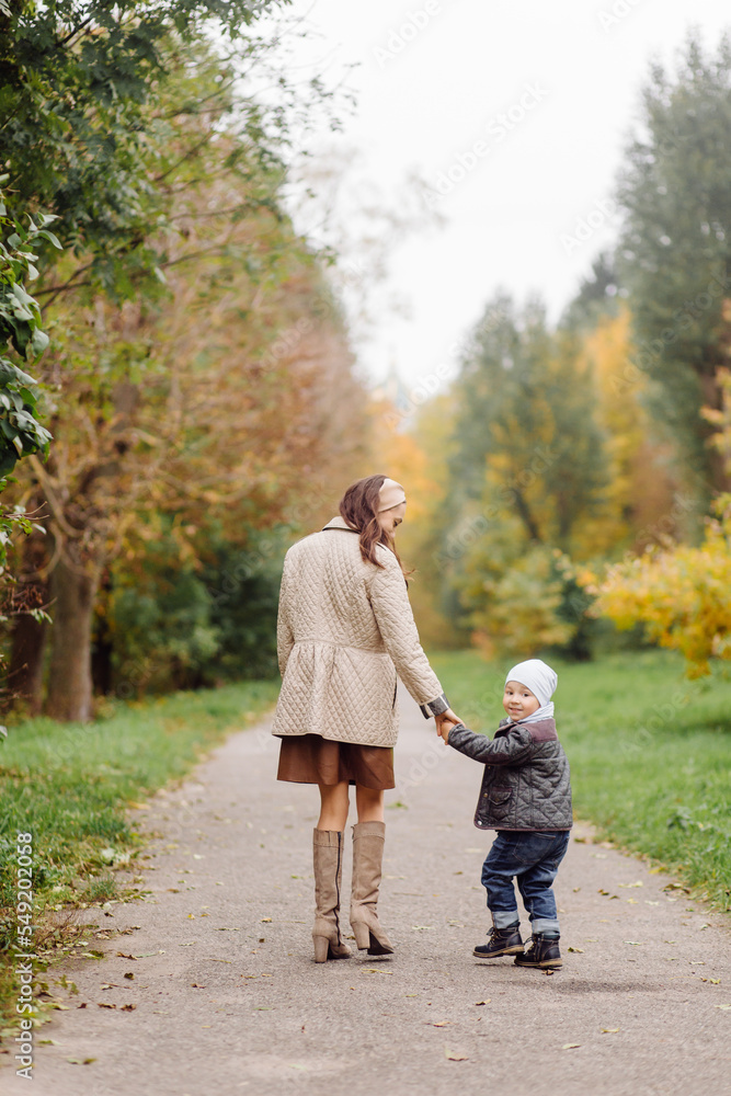 Fototapeta premium Mom and son walking and having fun together in the autumn park.