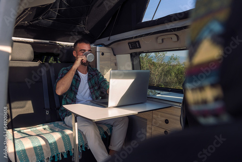 young man working on his laptop from his camper van, concept of freedom and digital nomad lifestyle photo