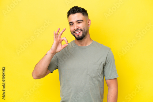 Young Arab handsome man isolated on yellow background showing ok sign with fingers