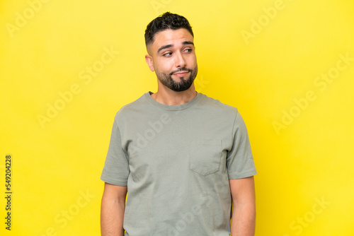 Young Arab handsome man isolated on yellow background making doubts gesture looking side