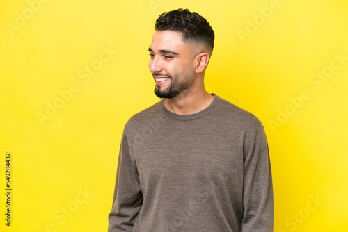 Young Arab handsome man isolated on yellow background looking to the side and smiling