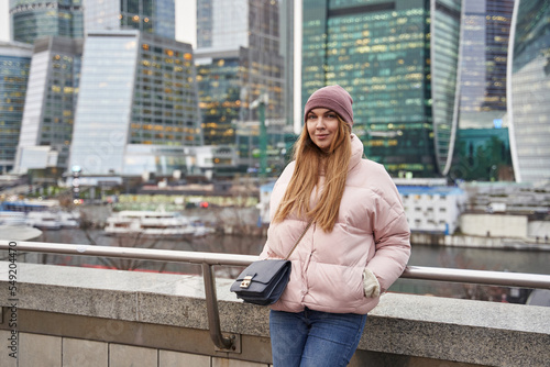beautiful woman in warm clothes next to skyscrapers and skyscrapers of a big city. tall glass business centers in the background.
