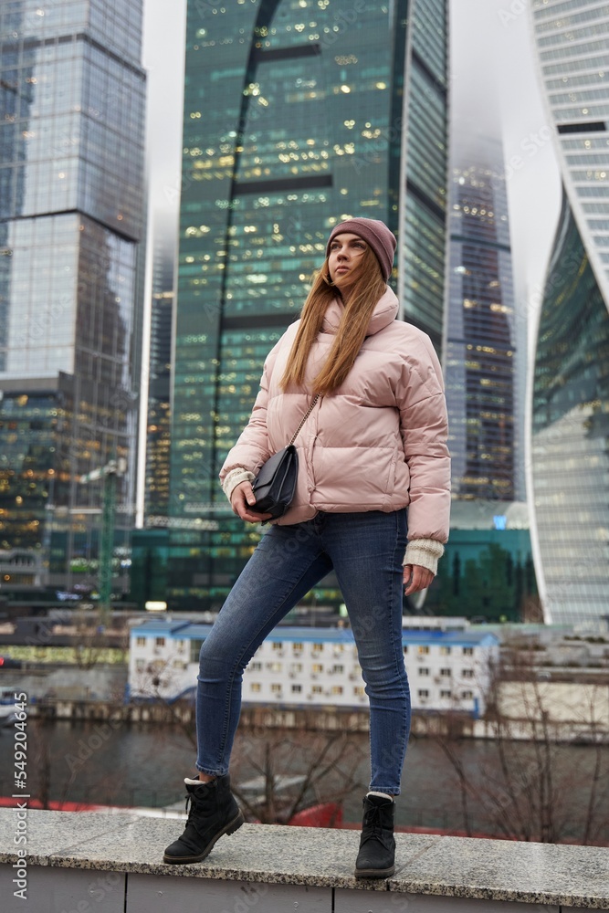 beautiful woman in warm winter clothes next to skyscrapers and skyscrapers of a big city. tall glass business centers in the background.