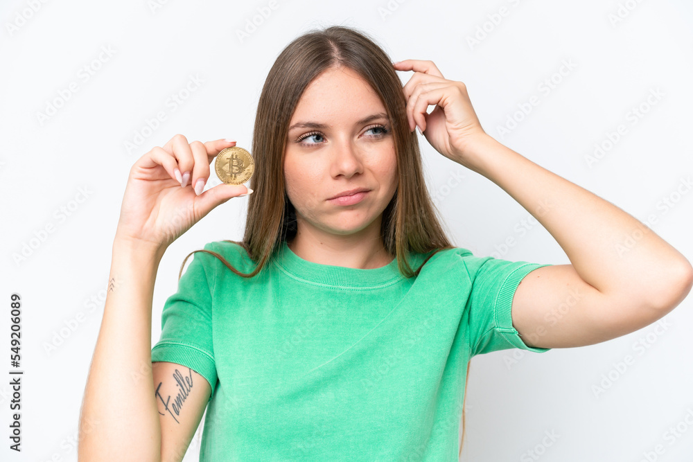 Young beautiful blonde woman holding a Bitcoin isolated on white background having doubts and with confuse face expression Young beautiful blonde woman holding a Bitcoin isolated on white background having doubts and with confuse face expression
