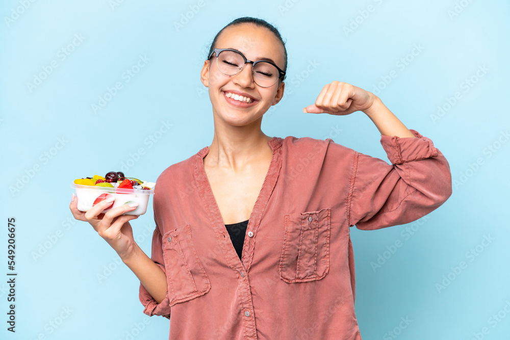 Young Arab woman holding a bowl of fruit isolated on blue background doing strong gesture Young Arab woman holding a bowl of fruit isolated on blue background doing strong gesture