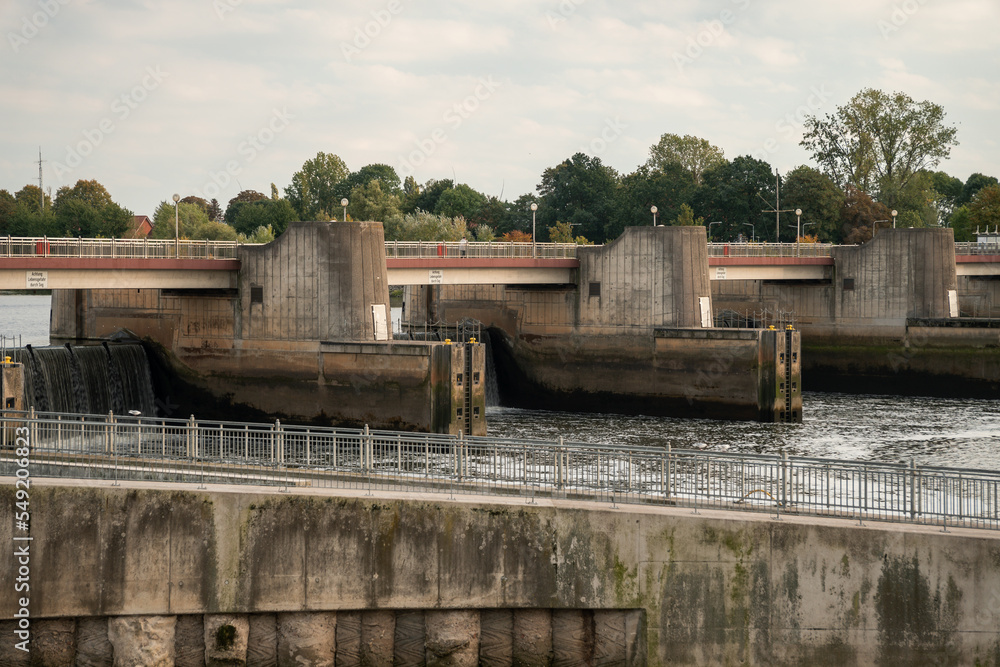 Dam (weir) of a hydro power plant along Weser river (Bremen). Water cascading down a barrage.  Weir called "Weserwehr". Dirty concrete. Translation of german sign: "Life danger because of suction". - obrazy, fototapety, plakaty 