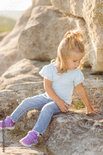 Beautiful mother and her cute long haired daughter are walking on meadow of stone