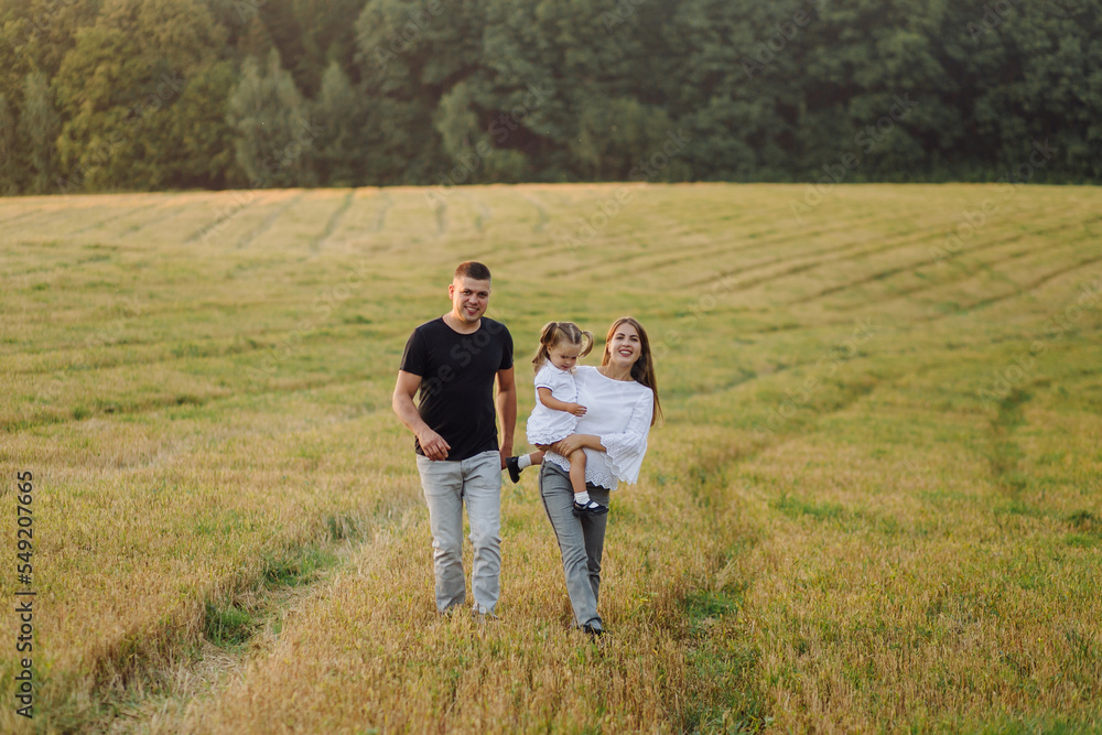 Happy family in a field in autumn. Mother, father and baby play in nature in the rays of sunset Happy family in a field in autumn. Mother, father and baby play in nature in the rays of sunset