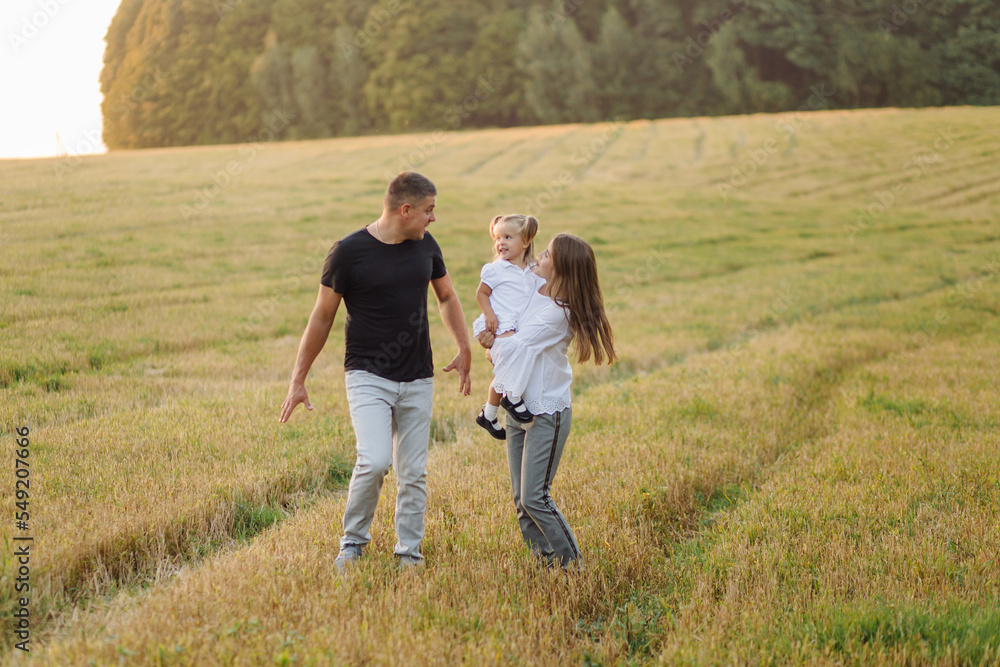 Happy family in a field in autumn. Mother, father and baby play in nature in the rays of sunset