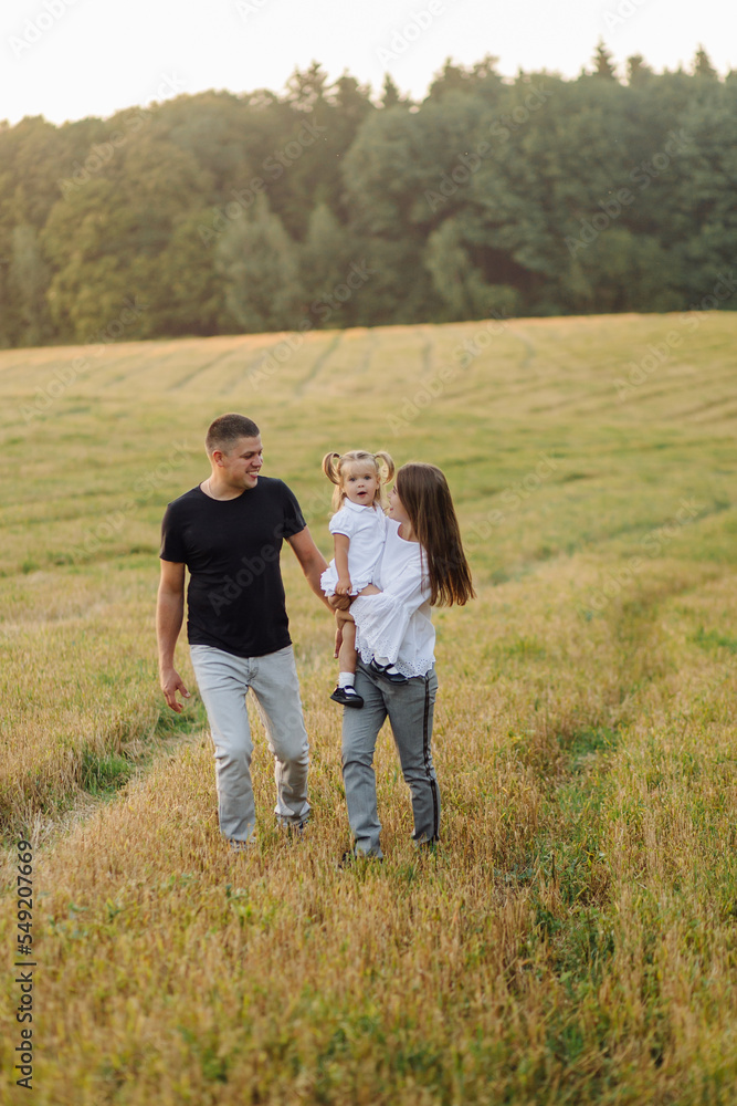 Happy family in a field in autumn. Mother, father and baby play in nature in the rays of sunset Happy family in a field in autumn. Mother, father and baby play in nature in the rays of sunset