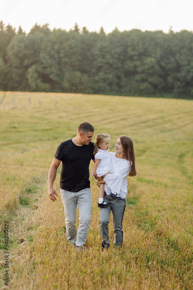 Happy family in a field in autumn. Mother, father and baby play in nature in the rays of sunset Happy family in a field in autumn. Mother, father and baby play in nature in the rays of sunset