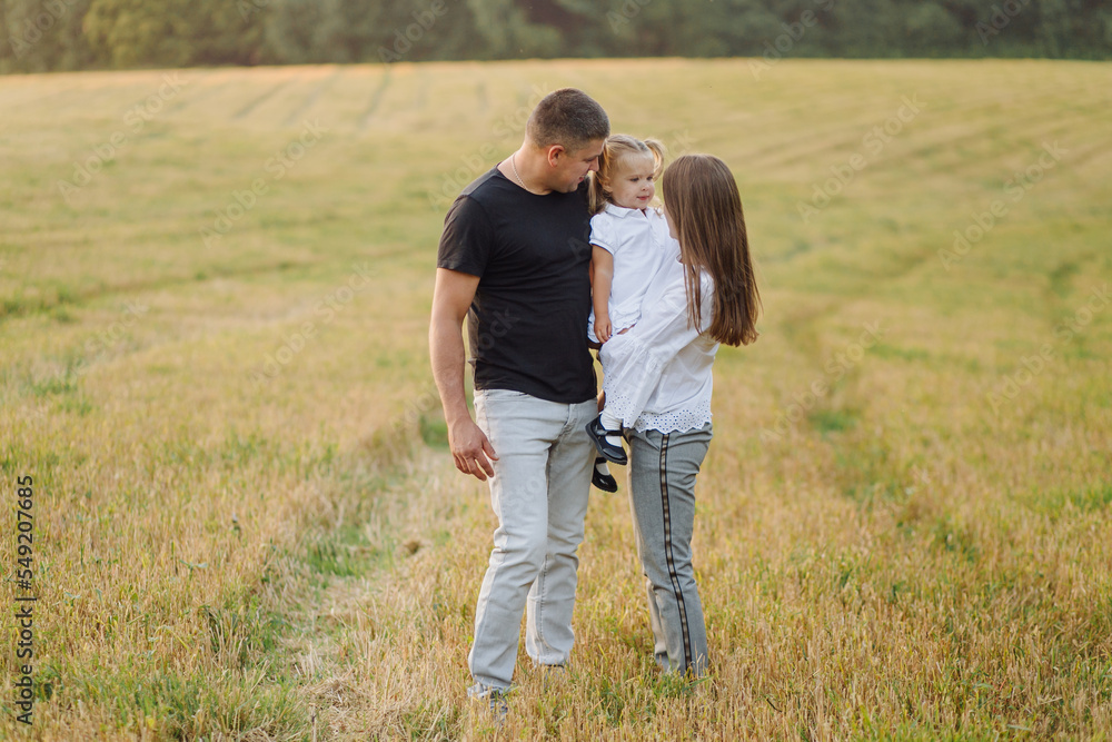 Happy family in a field in autumn. Mother, father and baby play in nature in the rays of sunset