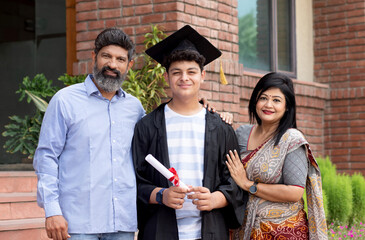 Happy Indian university boy student and proud parents celebrating graduation degree convocation ceremony