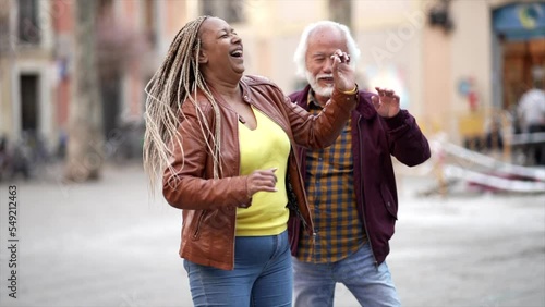 Multiracial senior couple dancing down a city street.