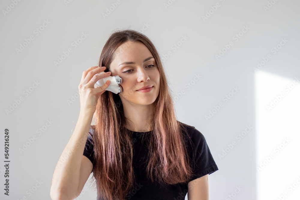 Happy woman doing facial microcurrents. Facial massage at home with a device with currents. Happy woman doing facial microcurrents. Facial massage at home with a device with currents.