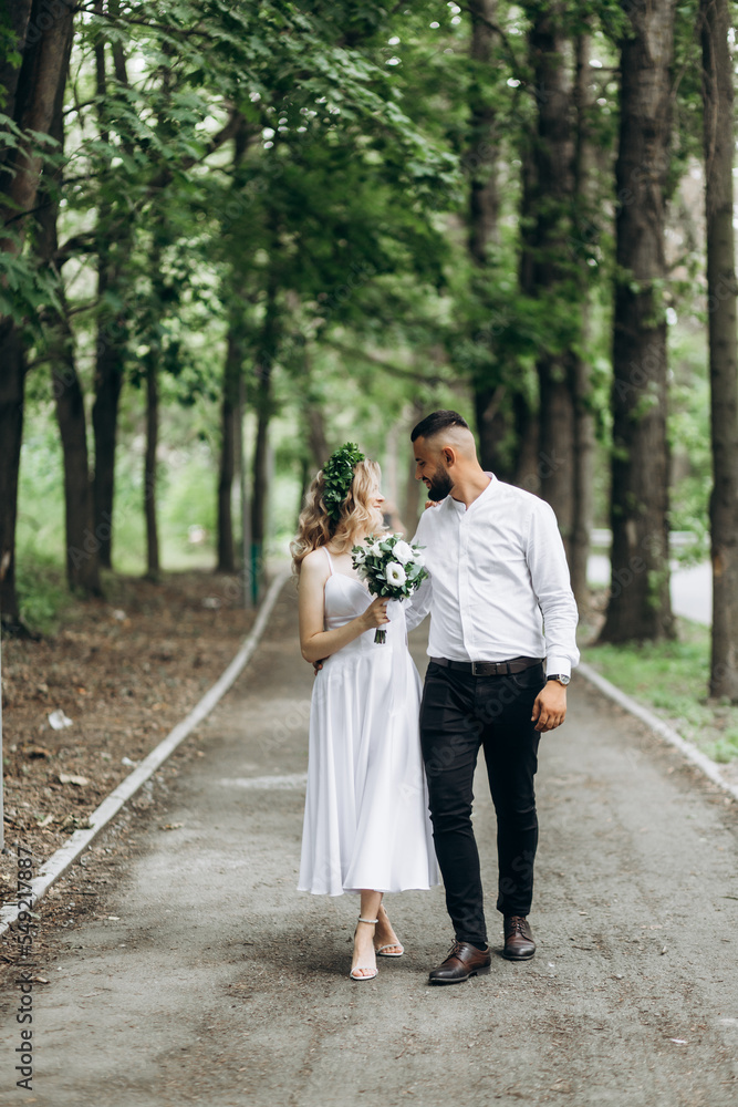Fototapeta premium A happy young couple in love walk in a garden. A man in a white shirt and a girl in a white light dress are walking in a park