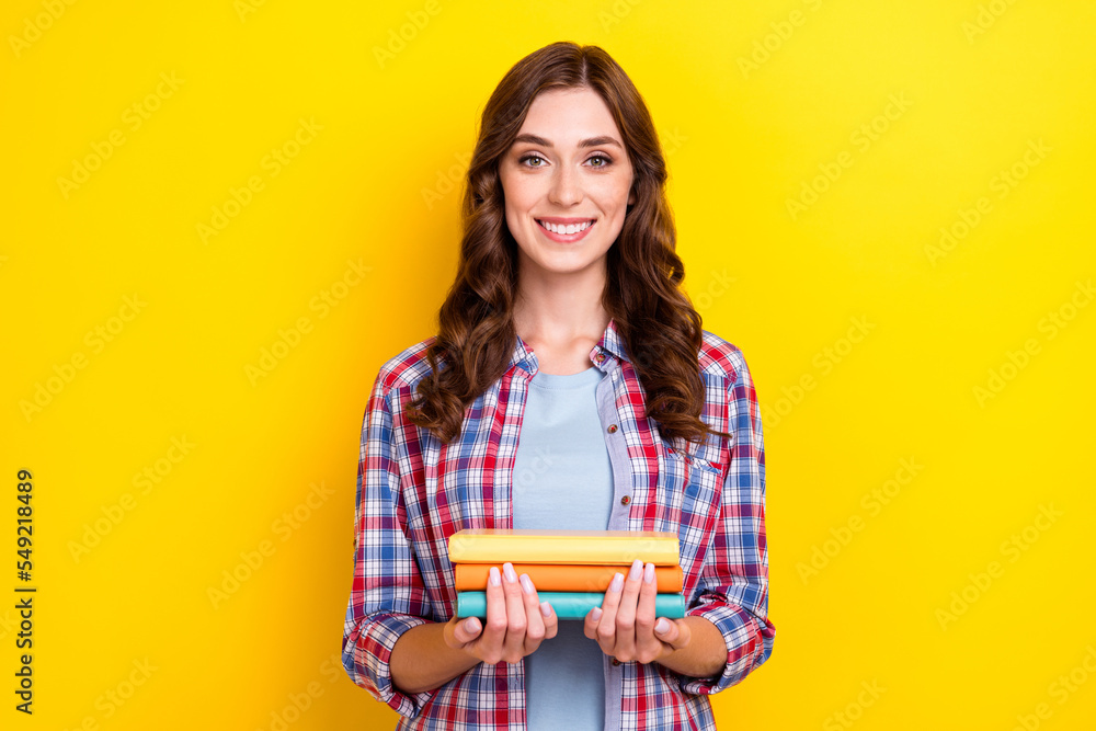 Portrait of satisfied intelligent nice woman with curly hairstyle wear checkered shirt hold book isolated on yellow color background Portrait of satisfied intelligent nice woman with curly hairstyle wear checkered shirt hold book isolated on yellow color background