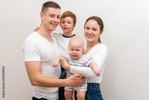 portrait of a young family, father, mother and two small sons, cheerful, friendly and strong family. They smile and hug children in their arms. The concept of a young friendly family 