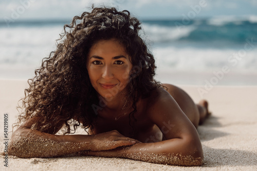Portrait of smiling latin woman with tanned body on beach. Sexy model girl lies on the sand at summer beach photo