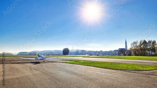 Ultraleichtflugzeug steht am Rollfeld auf einem Flugplatz an einem sonnigen Tag, Kleinstadt mit Krichturm im Hintergrund photo
