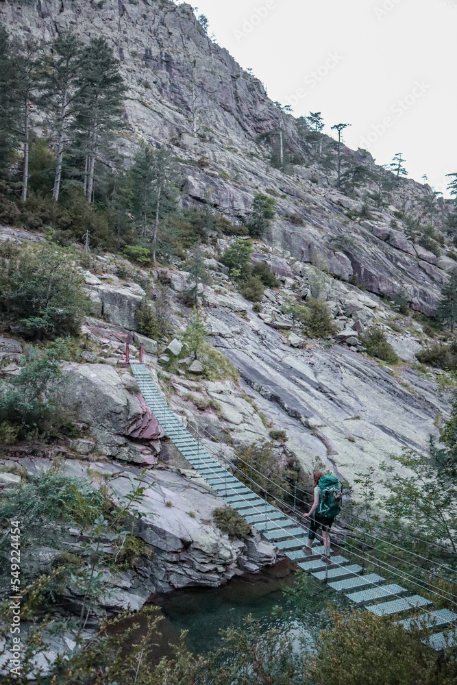 Woman crossing a hanging bridge during the GR20 in Corsica.