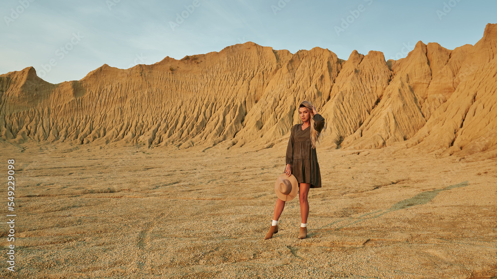 beautiful high sandy mountains and beautiful landscape. a young beautiful woman holds a hat in her hands and straightens her long blond hair