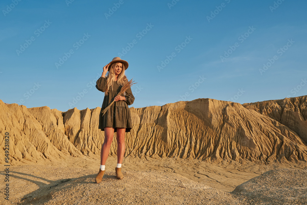 very beautiful tanned young beautiful woman with a bouquet of dry grass against the background of a blue sky and sandy cliffs and rock breaks