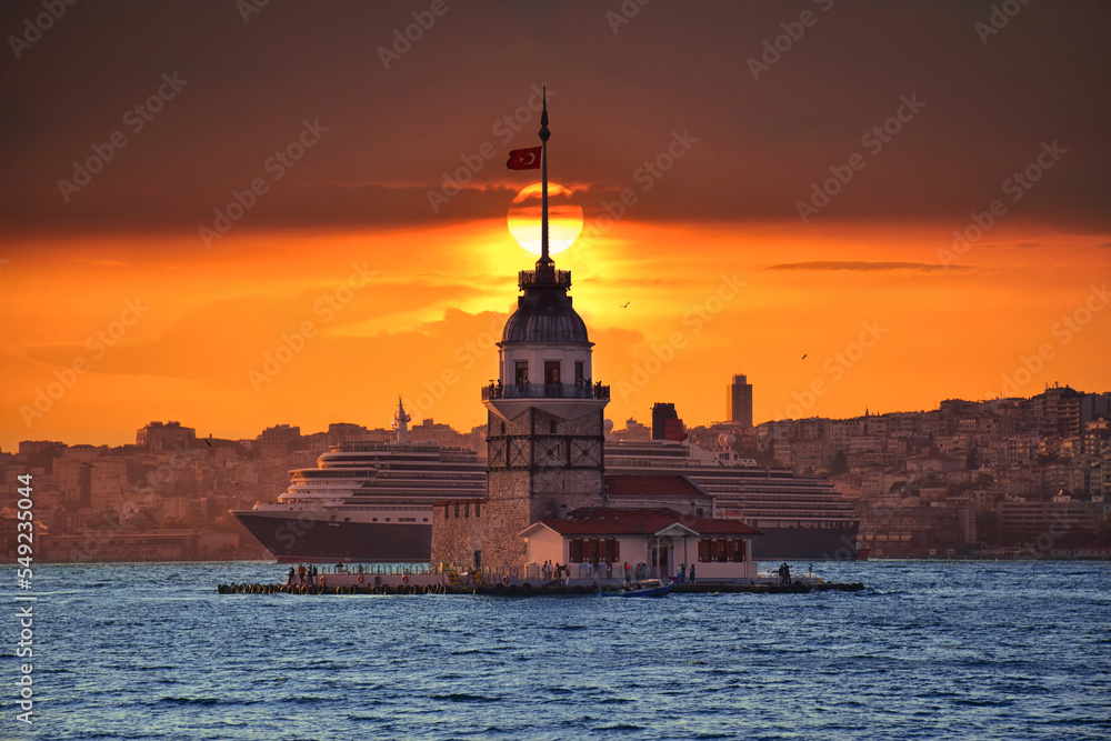 Fiery sunset over Bosphorus with famous Maiden's Tower (Kiz Kulesi) also known as Leander's Tower, symbol of Istanbul, Turkey. Scenic travel background and cruise ship for wallpaper or guide book.