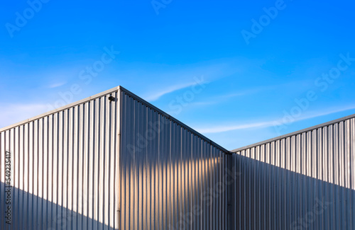 Corrugated Steel Wall of industrial Warehouse Building against blue sky background with sunlight and shadow on surface © Prapat